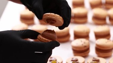 Process of making macarons macaroons, french dessert. chef hands in black gloves are assembling, connecting of two halves with chocolate stuffing at pastry shop. cooking, food and baking concept