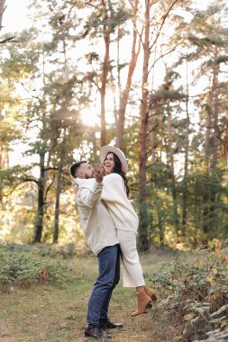 St. Valentines day. Happy young bearded man is carrying woman in hands in sunny park on warm day. Happy stylish loving couple enjoying date and celebrating anniversary outdoors at nature.