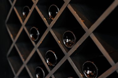 Kilerde, markette, restoranda ya da evdeki ahşap raflarda üst üste dizilmiş seçkin siyah şarap şişeleri. Şişe koleksiyonu Rafta şarap.