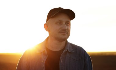 Şapkalı gülümseyen erkek çiftçinin portresi gün batımında sonsuz tarlalarda yürümektir. Günışığında ekilmiş toprakları araştıran profesyonel tarım uzmanı. Tarım sektörü kavramı ve tarım