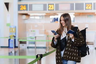 Seyahat, tatil, turizm. Havaalanı terminaline giriş yaptıktan sonra pasaportunu gösteren, gülümseyen, sırt çantası taşıyan mutlu ve çekici genç bir kadın turist..