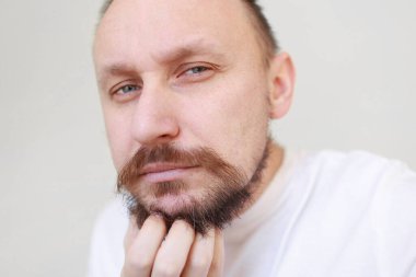 Kesilmiş atıcının eli dizginlenmemiş, tıraşsız çene kaşındırıyor. Kalın sakallı ve bıyıklı, beyaz tişörtlü, fazla büyümüş, çirkin bir erkek. Güzellik salonu konsepti, berber dükkanı..