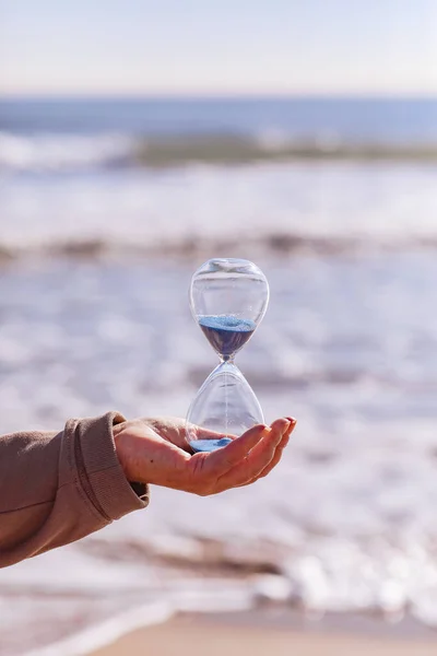 时间过得很快 成熟女人手中拿着蓝色沙子的沙漏 象征着生命的短暂 背景是有美丽阳光的大海 时间快速流逝的概念 复制空间 — 图库照片