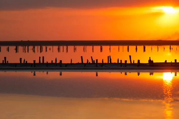 水の中で太陽の反射とビーチの上にオレンジの夕日 劇的かつ壮大な空 非常に塩辛い湖 ウクライナの塩抽出のための木の投稿 夏の季節 牧歌的な静かな夕暮れの日差し — ストック写真