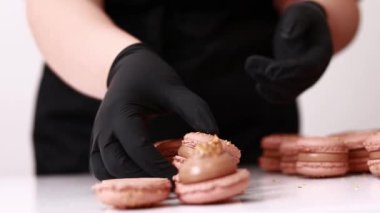 Process of making macarons macaroons, french dessert. chef hands in black gloves are assembling, connecting of two halves with chocolate stuffing at pastry shop. cooking, food and baking concept