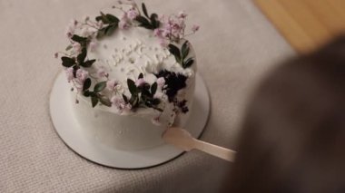 Tanınmayan küçük bir kız çocuğu ahşap kaşık süslenmiş çiçeklerle doğum günü pastasıyla beyaz krem ve keten doğal masa örtüsüne yazılan mutlu yıllar pastasıyla yemek yiyor..