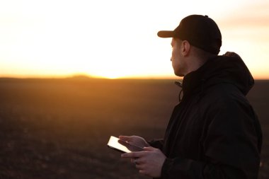 Akıllı tarım teknolojisi ve tarım. Çiftçi gün batımında toprakla tarlada dijital tablet kullanır. Toprak kalitesinin kontrol ve kontrolü, ekin ekmeye ve sebze ekmeye hazır arazi.