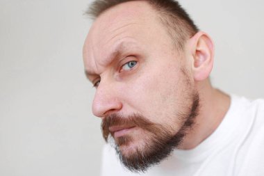 Kesilmiş atıcının eli dizginlenmemiş, tıraşsız çene kaşındırıyor. Kalın sakallı ve bıyıklı, beyaz tişörtlü, fazla büyümüş, çirkin bir erkek. Güzellik salonu konsepti, berber dükkanı..