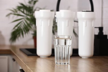 Mutfaktaki ahşap masa üstünde bir bardak temiz içme suyu ve filtre kartuşları. Ev bitkisi. Ters osmoz su arıtma sistemi kurulumu. Konsept ev filtreleme sistemi.