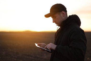 Akıllı tarım teknolojisi ve tarım. Çiftçi gün batımında toprakla tarlada dijital tablet kullanır. Toprak kalitesinin kontrol ve kontrolü, ekin ekmeye ve sebze ekmeye hazır arazi.