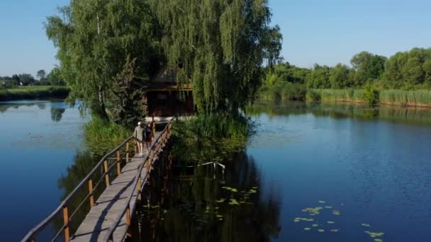島の古い木造漁師とハンターの家 湖のキャビンに古い木製の橋の上を歩いて手を携えて愛のカップルと風景 旧ソロトビン村 ウクライナ — ストック動画