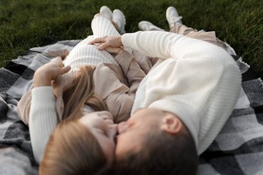 Mutlu aile günleri. Karı koca kucaklaşır, yatar ve çimlerin üzerinde öpüşürler. Anneler Günü. Babalar Günü. Hamilelik, ebeveynlik, annelik, aşk konsepti