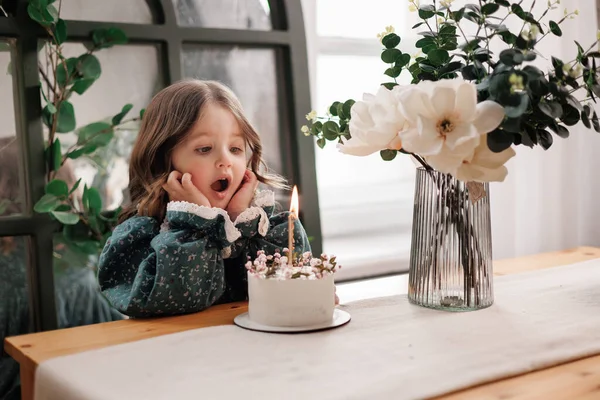 子供の誕生日パーティー 愛らしい少女は 誕生日ケーキ装飾された花と燃えるキャンドルでテーブルに座って 願い事をします 風船のある部屋でお祝いのドレスの子供 花瓶の花の花束 — ストック写真
