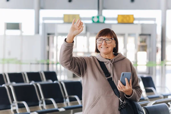 Szczęśliwy Uśmiechnięty Dojrzały Podróżnik Kobieta Trzymać Smartfona Machać Ręką Powitaniu — Zdjęcie stockowe