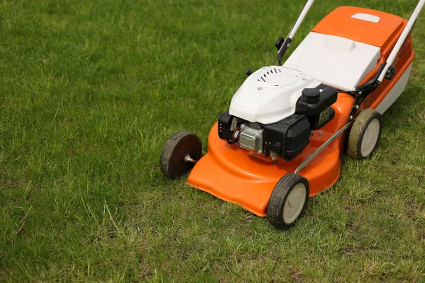 stock image Top view of modern orange-grey electric lawn mower cutting bright lush green grass. Gardening work tools. Rotary lawn mower machine on lawn. Professional lawn care service. Place for text.
