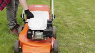 Koruyucu eldivenli tanınmayan bahçıvan arka bahçesindeki yeşil çimleri biçmeden önce çim biçme makinesini çalıştırıyor. Motosikletli çim biçme makinesi olan adam bahçe düzenlemesi ile ilgileniyor..