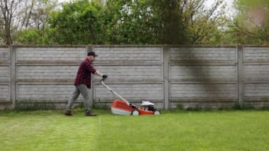 Sıradan giysiler içinde bir adam evinin arka bahçesinde çim biçme makinesiyle çim biçiyor. Baharın bulutlu olduğu bir günde koca bahçeyle ilgilenir. Modern benzin bahçesi ekipmanları. Peyzaj işi.