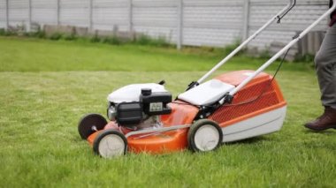 Tanımlanamayan bir erkek, gündelik giysiler içinde modern benzin kablosuz çim biçme makinesini itiyor, evinin arka bahçesindeki yeşil çimenleri buduyor ve umursuyor. Bahçe bakımı aletleri ve ekipmanları.