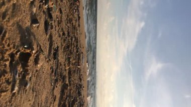 Kumlu sahillerde deniz aşırı su dalgaları ve gündüz bulutlu gökyüzü. Dikey video. Tropikal manzara.