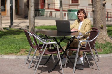 Zarif yetişkin iş kadını laptopta çalışır ve daktilo eder. Şehirdeki açık bir kafede akıllı telefondan arama yapar. Kamu alanından uzak iş iletişimi kavramı, dijital serbest çalışma, modern yaşam tarzı