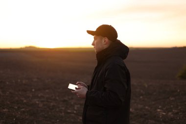 Akıllı tarım teknolojisi ve tarım. Çiftçi gün batımında toprakla tarlada dijital tablet kullanır. Toprak kalitesinin kontrol ve kontrolü, ekin ekmeye ve sebze ekmeye hazır arazi.