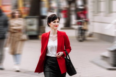 Resmi giyimli, kırmızı ceketli, kendine güvenen genç iş kadını şehir caddesinde yürürken telefonla konuşuyor. İş konsepti için telekomünikasyon ve mobil ağ. Kadın İş Biçimi.