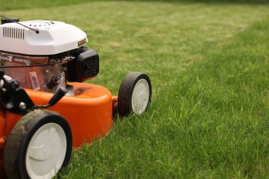 Bahçıvanlık aletleri. Turuncu elektrikli çim biçme makinesi, tekerlekler, parlak yemyeşil çimlerdeki motor detaylarını kapat. Döner çim biçme makinesi çimleri kesti. Profesyonel bahçe bakımı servisi. Metin için yer.