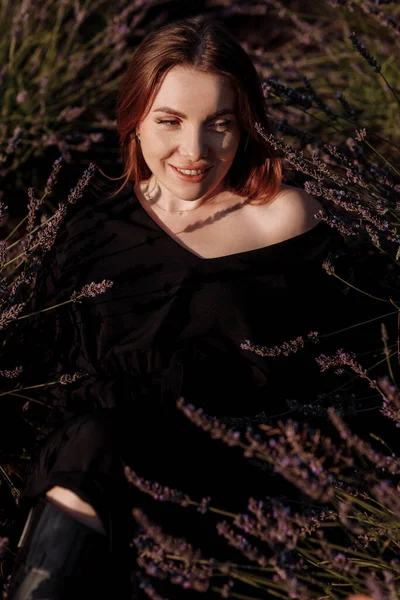 穿着黑色衣服的年轻性感女子的画像是坐在盛开芬芳的紫色薰衣草地里 看着相机 迷人的黑发女孩享受着生活和梦想 自然美概念 — 图库照片