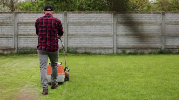 在他家后院 穿着休闲装的男人用割草机割草的背景图 春天多云的日子 丈夫照顾花园 现代汽油花园设备 景观美化工作 — 图库视频影像