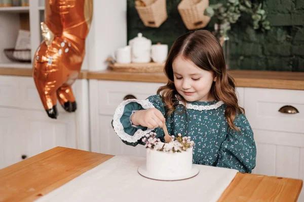 誕生日パーティーだ ハッピーかわいい子供の女の子4 5年はお祝いのドレスを身に着けている喜びエコ木製スプーンで食べています彼女の装飾された花お弁当の誕生日ケーキで白いクリームでスタイリッシュな家庭のキッチン — ストック写真