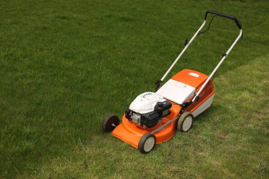 Modern turuncu-gri çim biçme makinesinin parlak yemyeşil çimleri biçme manzarası. Bahçıvanlık aletleri. Çimenlikteki çim biçme makinesi. Profesyonel bahçe bakımı servisi. Metin için yer.