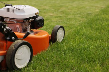 Bahçıvanlık aletleri. Turuncu elektrikli çim biçme makinesi, tekerlekler, parlak yemyeşil çimlerdeki motor detaylarını kapat. Döner çim biçme makinesi çimleri kesti. Profesyonel bahçe bakımı servisi. Metin için yer.