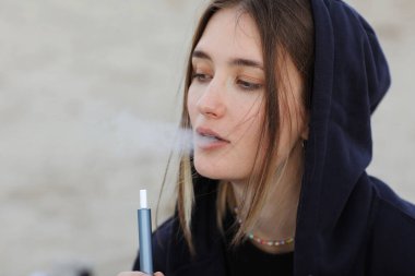 Elektronik sigara teknolojisi. Genç bir kadın sigara içiyor ve hibrit sigara cihazından buhar çıkarıyor. Gerçek tütün doldurma yastığı ve tütün ısıtma sistemi kullanıyor. Kötü kötü alışkanlık.