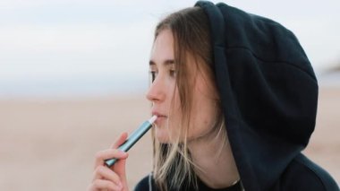Elektronik sigara teknolojisi. Genç bir kadın sigara içiyor ve hibrit sigara cihazından buhar çıkarıyor. Gerçek tütün doldurma yastığı ve tütün ısıtma sistemi kullanıyor. Kötü kötü alışkanlık.