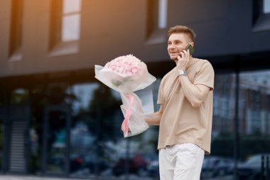Çiçek teslimatı. Elinde bir buket ortanca çiçeği olan gülümseyen teslimatçı müşterisiyle modern apartmanda akıllı telefondan konuşuyor. Sevgililer günü, doğum günü, yıldönümü hediyesi..
