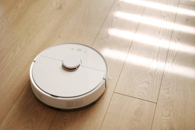 Beyaz kablosuz otonom robot elektrikli süpürgenin ahşap zemindeki en üst görüntüsü. Akıllı temizlik teknolojisi. Otomatik itişli temizlik robotu. Yer temizleme sistemi. Ev kumandası aygıtları