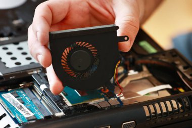 Laptop tamir ediliyor. Tamirci soğutma vantilatörü ve aşırı ısınmadan dolayı onarım yapıyor. Bilgisayarı sökmek, yenisini almak, temiz toz ve deftere toprak soğutma sistemi koymak. Profesyonel elektronik cihaz servisi.