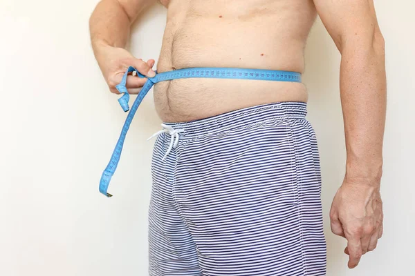 A man measures his fat belly with measuring tape. Concept of weight loss, health problems of obese people. Poor nutrition and sedentary lifestyle. Increased risk of heart illnesses. World Obesity Day.