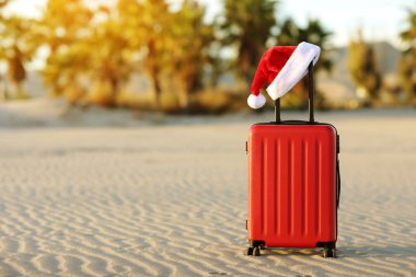 İçinde Noel Baba 'nın kırmızı şapkası olan kırmızı bavul tropikal kumsal, palmiyeler, dağlar ve deniz altyapısı olan. Noel tatili ve yeni yıl için seyahat konsepti. Mesaj için yer. İndirimli geziler.