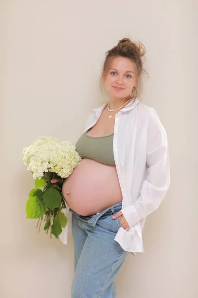 健康的な妊娠 腹の大きい妊婦さんが手にしている様子を横から眺めます 花の花束を持ってる女の子 テキストのスペースをコピーします 優雅な母親が赤ちゃんを待っている 選択的焦点 — ストック写真