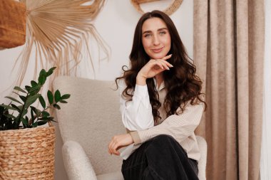 Çekici, kendine güvenen, şık, uzun saçlı esmer kadın kırsal tarzda yaratıcı tasarımı olan oturma odasına bakıyor. Güzellik, moda, kendini ifade etme, bireysellik kavramı