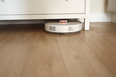 Kablosuz otonom robot elektrikli süpürge süpürgesi oturma odasında klozet altında fırçalarla süpürülüyor. Otomatik itişli temizlik robotu. Ev kumandası aletleri. Akıllı temizlik teknolojisi
