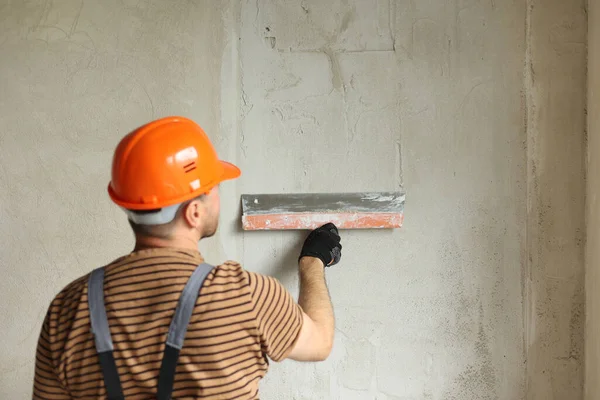 Tulum giymiş tamirci ve koruyucu miğfer takmış, macun bıçağıyla beton duvarları sıva ile sıvanmış. Dairenin yenilenmesi ve yeni bina konsepti