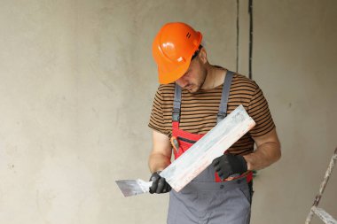 Tulumlu ve güvenlik şapkalı işçiler iki spatulayı macunla sıva yapmak için tutuyor ve hazırlıyorlar. Yenileme dairesi ve inşaat konsepti. Yer kopyala.