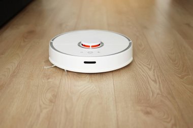 Beyaz kablosuz otonom robot elektrikli süpürgenin ahşap zemindeki en üst görüntüsü. Akıllı temizlik teknolojisi. Otomatik itişli temizlik robotu. Yer temizleme sistemi. Ev kumandası aygıtları