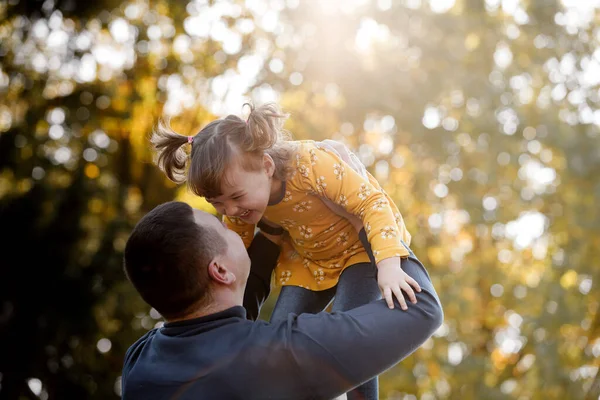 Happy fathers day. Joyful dad throws up his little smiling daughter at autumn park. Single daddy and child have fun, laugh and enjoy nature. Concept of parental care and happy carefree childhood.