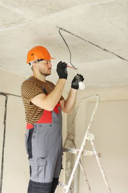 Üniformalı elektrik, koruyucu eldivenler ve tornavida ile elektrik voltajının kontrol edilip ölçülmesi. Yeni binadaki kabloları voltaj dedektörüyle inceliyorum..