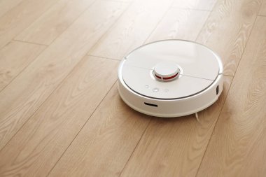 Beyaz kablosuz otonom robot elektrikli süpürgenin ahşap zemindeki en üst görüntüsü. Akıllı temizlik teknolojisi. Otomatik itişli temizlik robotu. Yer temizleme sistemi. Ev kumandası aygıtları