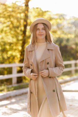 photo of pregnant woman holds hands on belly in the autumn park. Young woman in maternity warm dress and coat waiting for baby birth. Pregnancy, motherhood, mothers day. Happy pregnancy