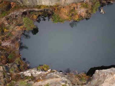 Kuzey Ukrayna 'nın Zhytomyr ilçesinde Korostyshiv granit ocağında bulunan kozalaklı bir sonbahar ormanının ortasındaki zümrüt göl ve kayaların manzarası. Zhytomyr Kanyonu.